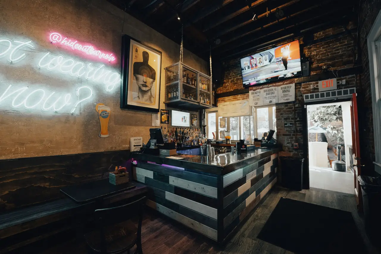 A corner of the front bar with a framed portrait, TVs and a white neon sign on the wall