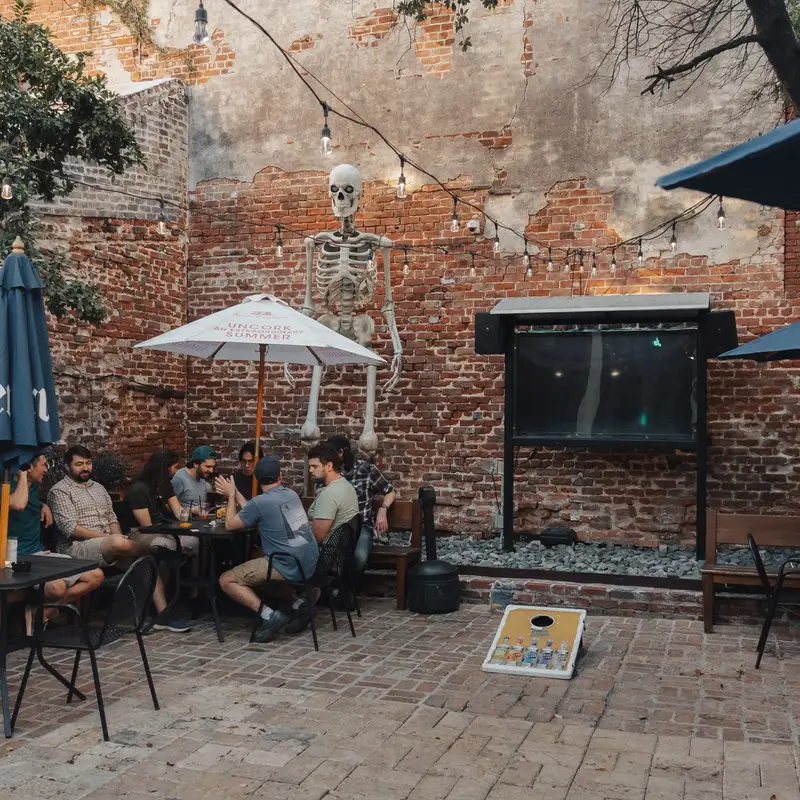 Guests at a table in the courtyard, with umbrellas, string lights and a cornhole board on the pavers