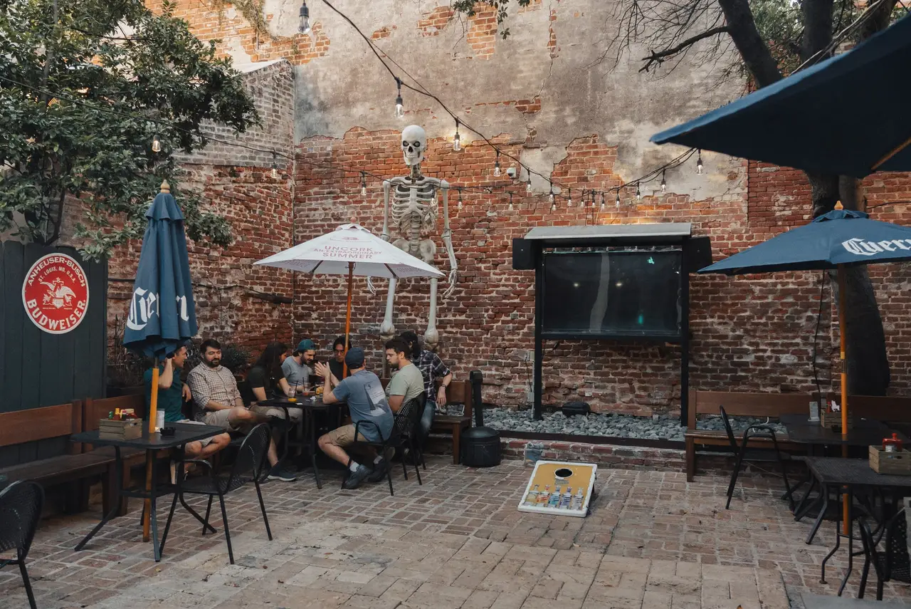 Guests at a table in the courtyard, with umbrellas, string lights and a cornhole board on the pavers