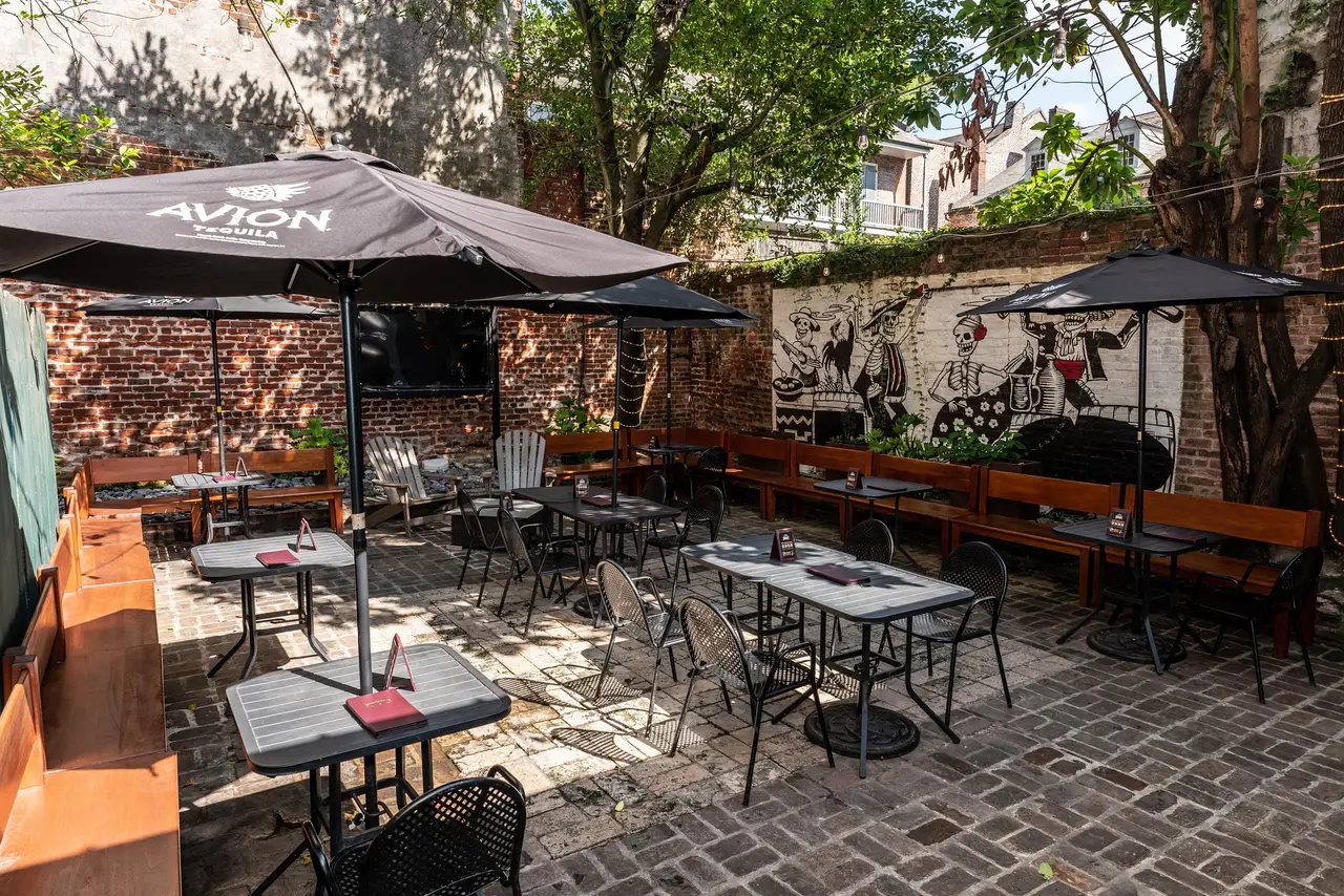 The Hideout’s brick courtyard in the sun: tables, chairs and umbrellas under the trees, with old brick walls all around