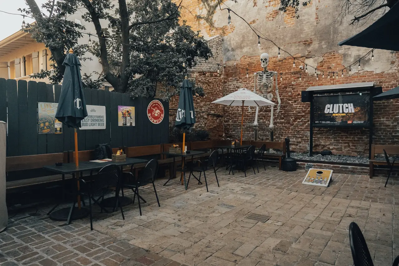 A wide view of the courtyard: umbrellas, tables along the walls and string lights over the brick