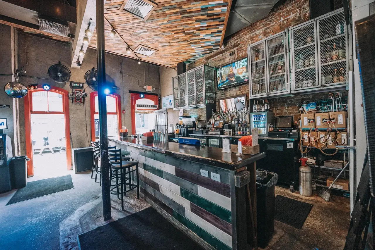 The front bar in daylight: a long bar with stools, glass-front cabinets and red doors open to Bourbon Street