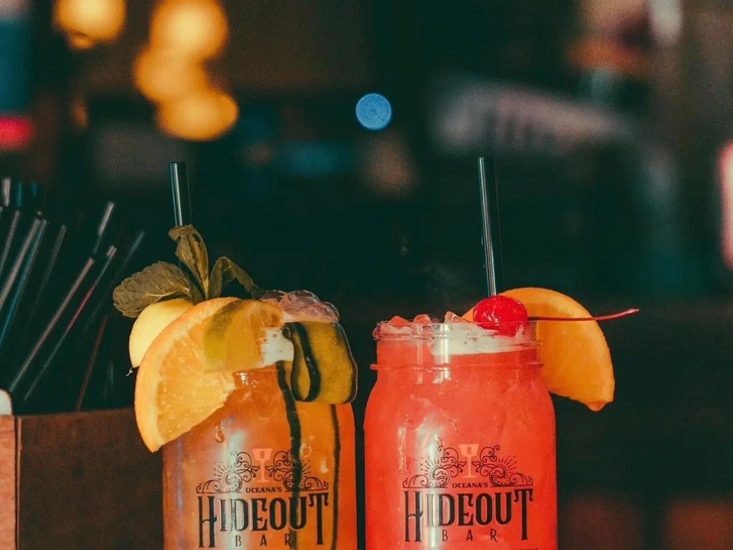 Two fruity cocktails garnished with orange and cherry in Hideout Bar mason jars