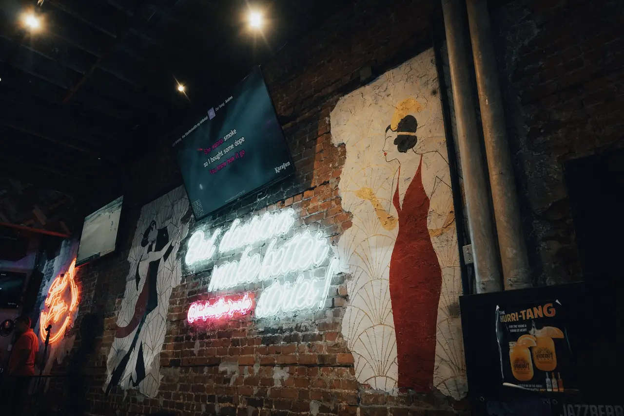 A mural of a woman in a red gown and a neon script sign on the brick wall of the bar