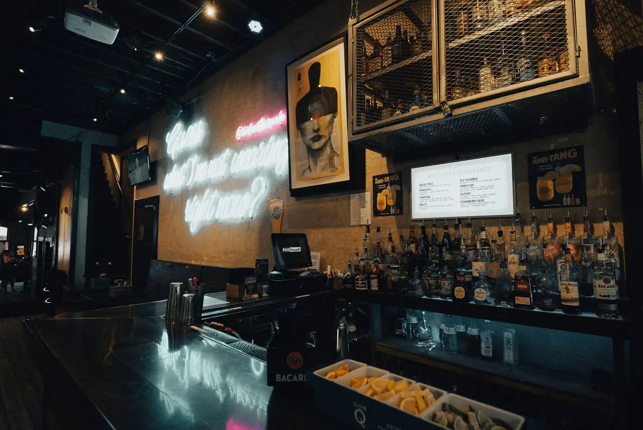 The back bar under a white neon script sign, a framed portrait and shelves of bottles