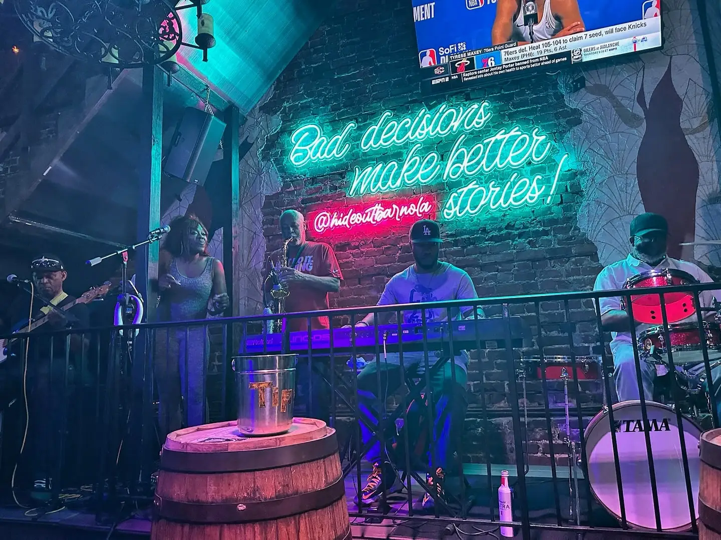 A band on stage under the “Bad decisions make better stories!” neon sign